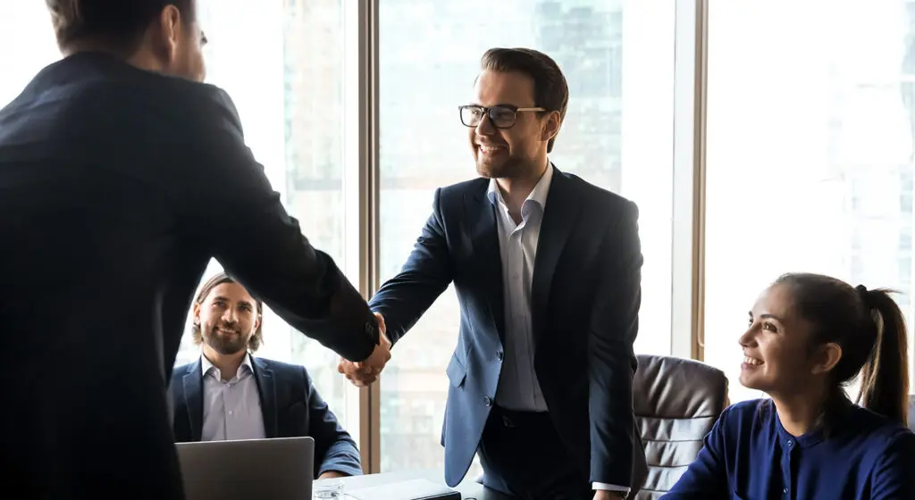 Two men wearing suits shaking hands in an office.
