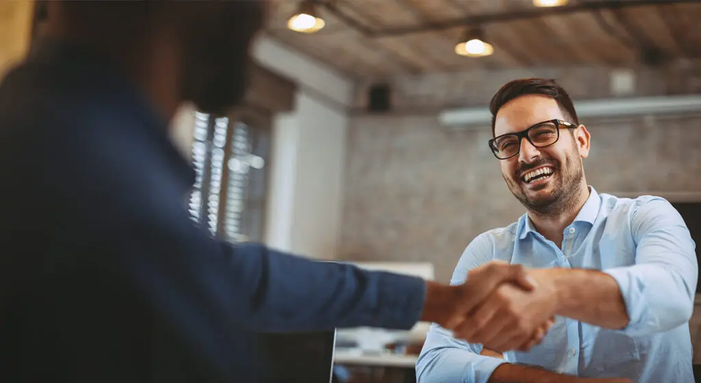 businessman smiling and shaking the hand of another person
