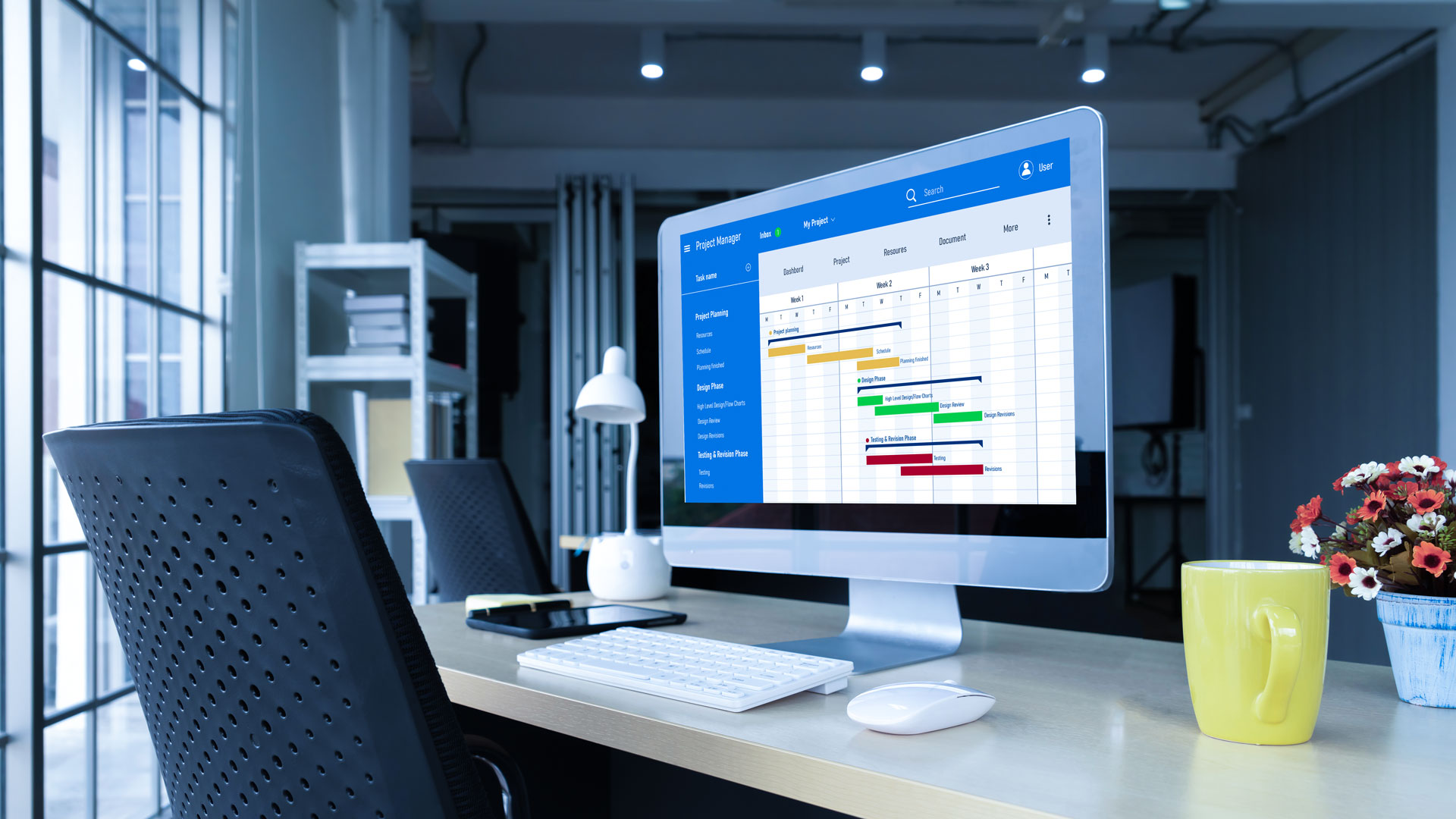 An empty desk and a computer monitor on the screen showing a project status