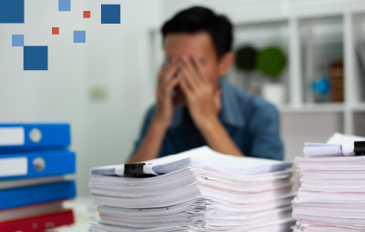 person rubbing eyes and appearing stressed with a large pile of paperwork in front of them