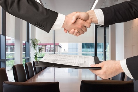 Close-up of two men in suits shaking hands in an office.