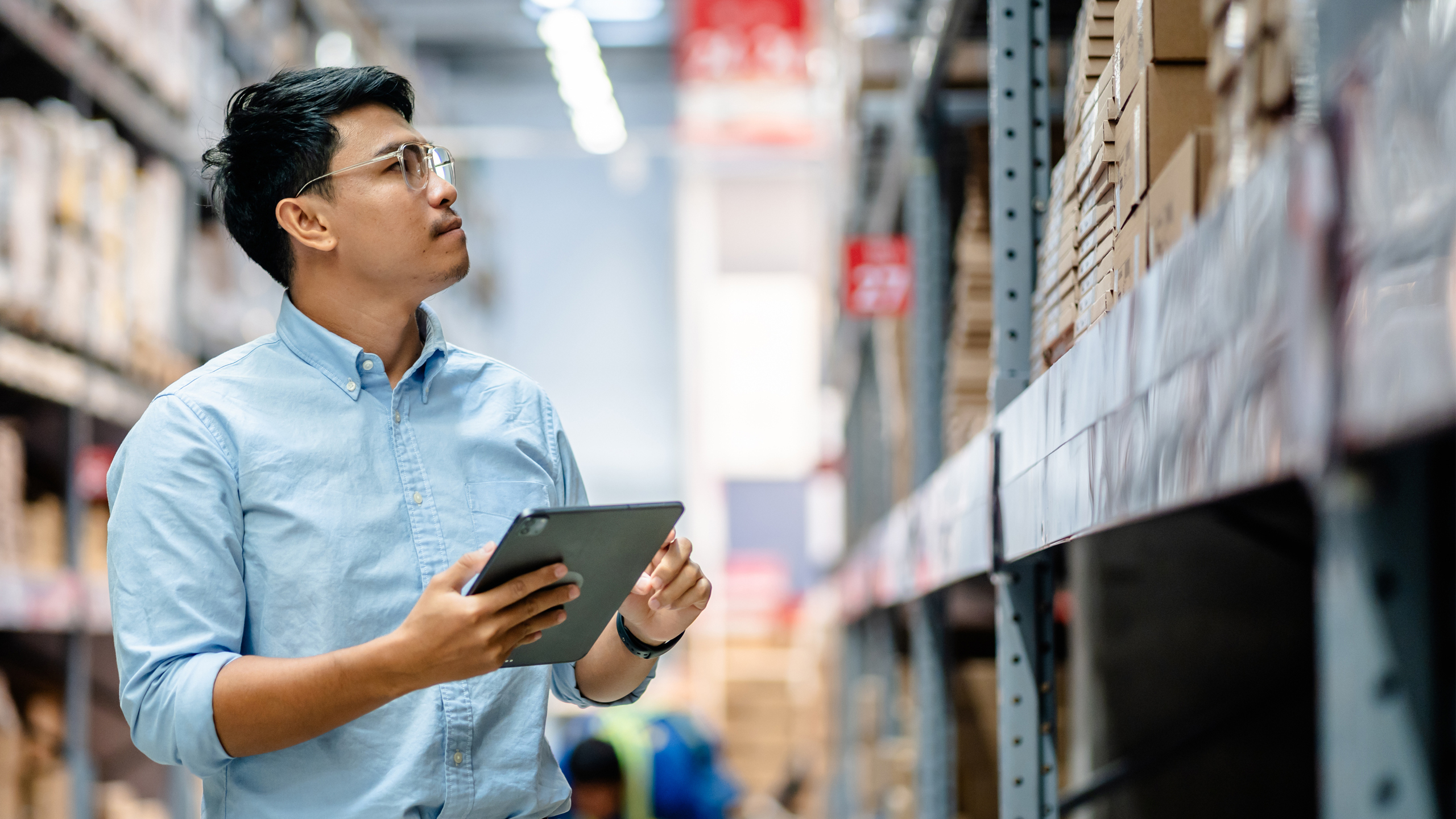 Distributor stands in warehouse holding a tablet while examining inventory