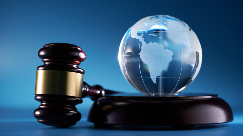 Glass globe sits on a table next to a gavel indicating law and global compliance