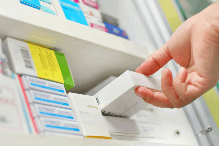 Close-up hand reaches onto a medical supply shelf and removes a box of prescription medication