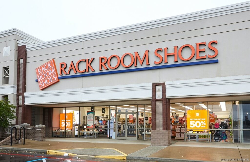 Rack Room Shoes storefront with large orange sign and blue accent, glass entrance, and sale posters visible inside the mall-style shopping center.
