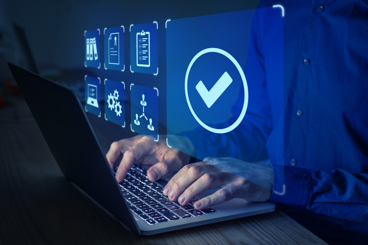 Person typing on a laptop with a large blue checkmark and floating blue icons symbolizing security and approval.
