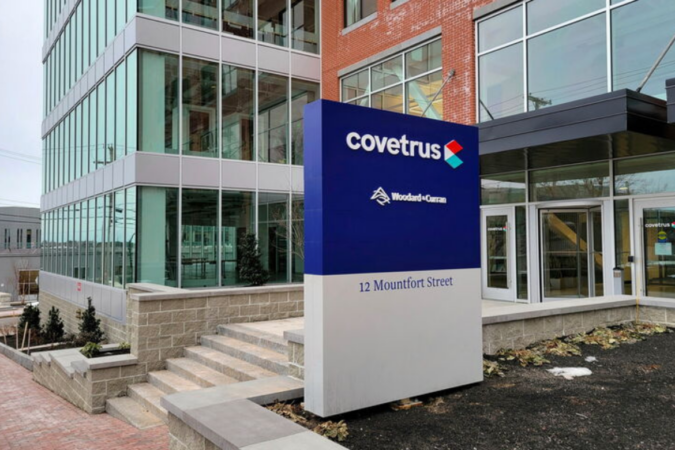 Exterior view of a modern office building with a tall blue Covetrus sign reading '12 Mountfort Street' in front of glass windows and brick facade.