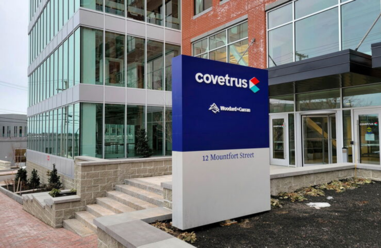 Exterior view of a modern office building with a tall blue Covetrus sign reading '12 Mountfort Street' in front of glass windows and brick facade.