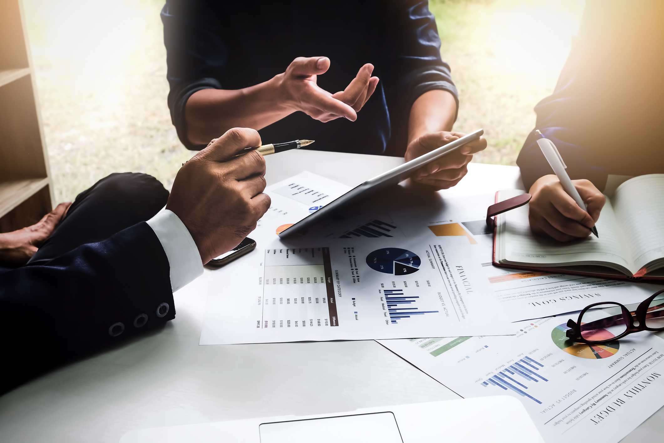 Hands of businesspeople reviewing financial charts and graphs on a table, with a tablet and notebook nearby