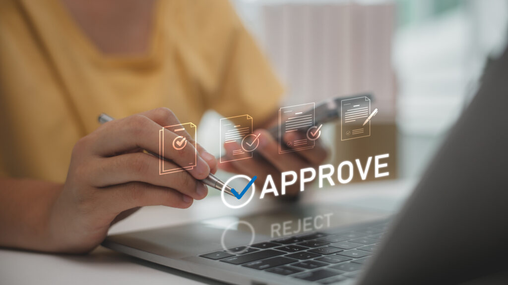 Close-up of a hand signing on a laptop with floating approval icons and the word APPROVE.